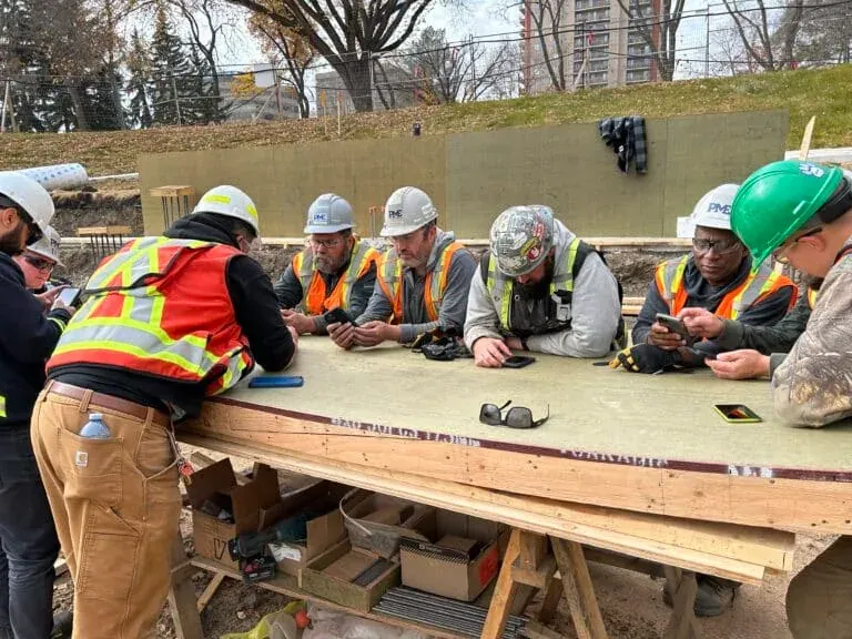 PME crew using Crewscope mobile app on phones during weekly work-plan review at jobsite table