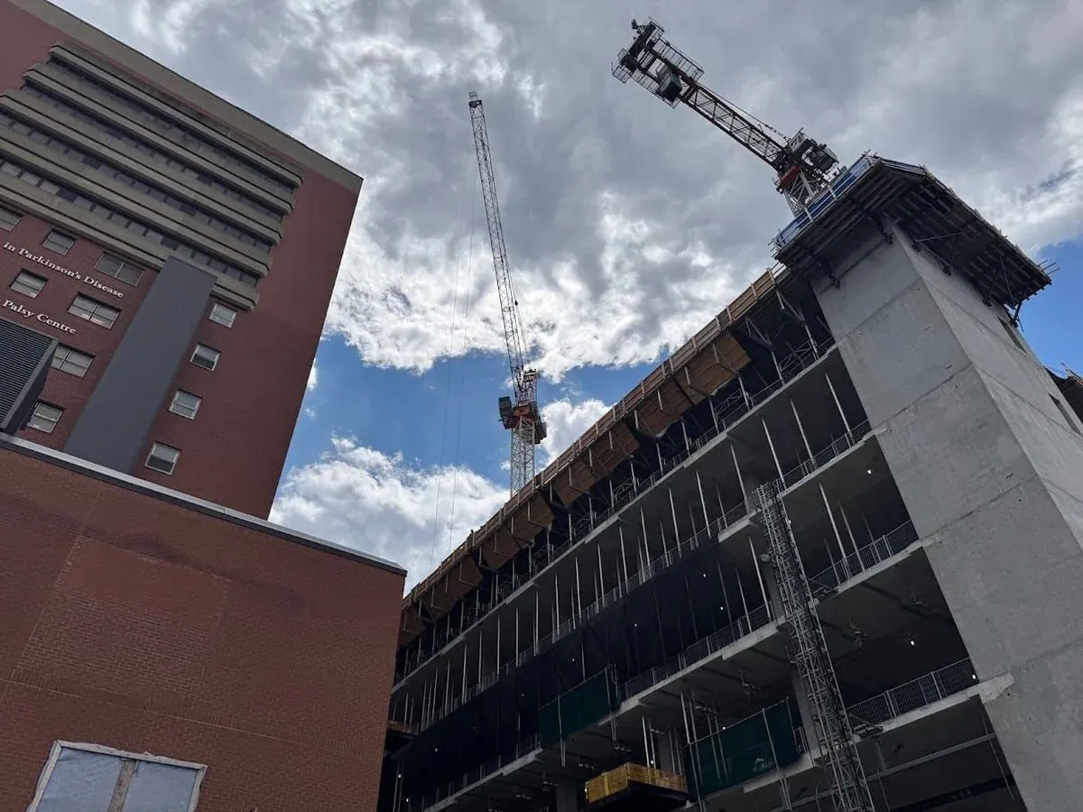 Crane and concrete building frame beside a brick hospital building at an EllisDon site