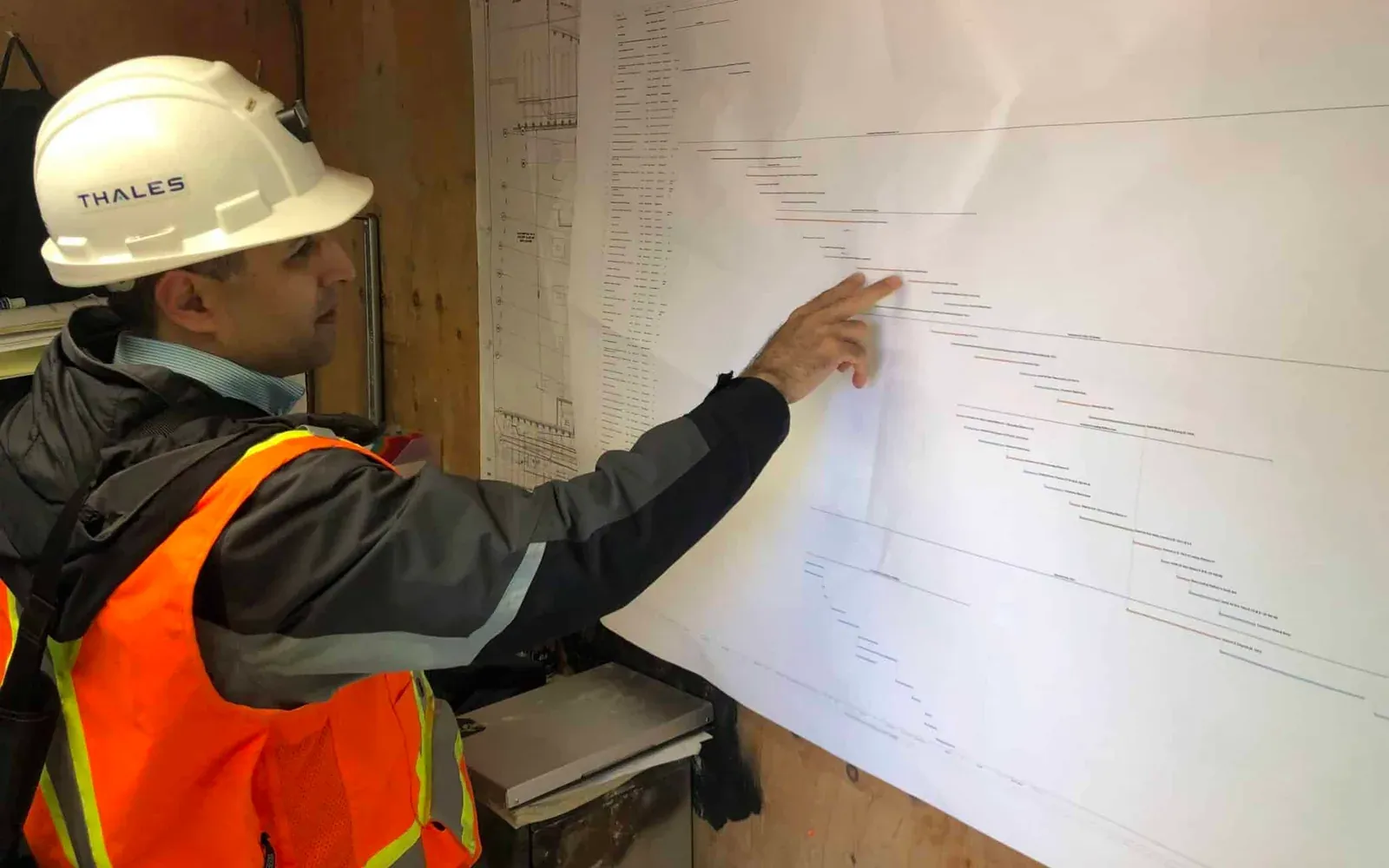 Construction superintendent in Thales hard hat pointing at a printed project Gantt schedule