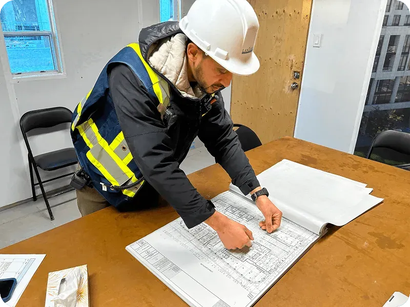 Construction supervisor in a hard hat reviewing blueprints at an on-site office