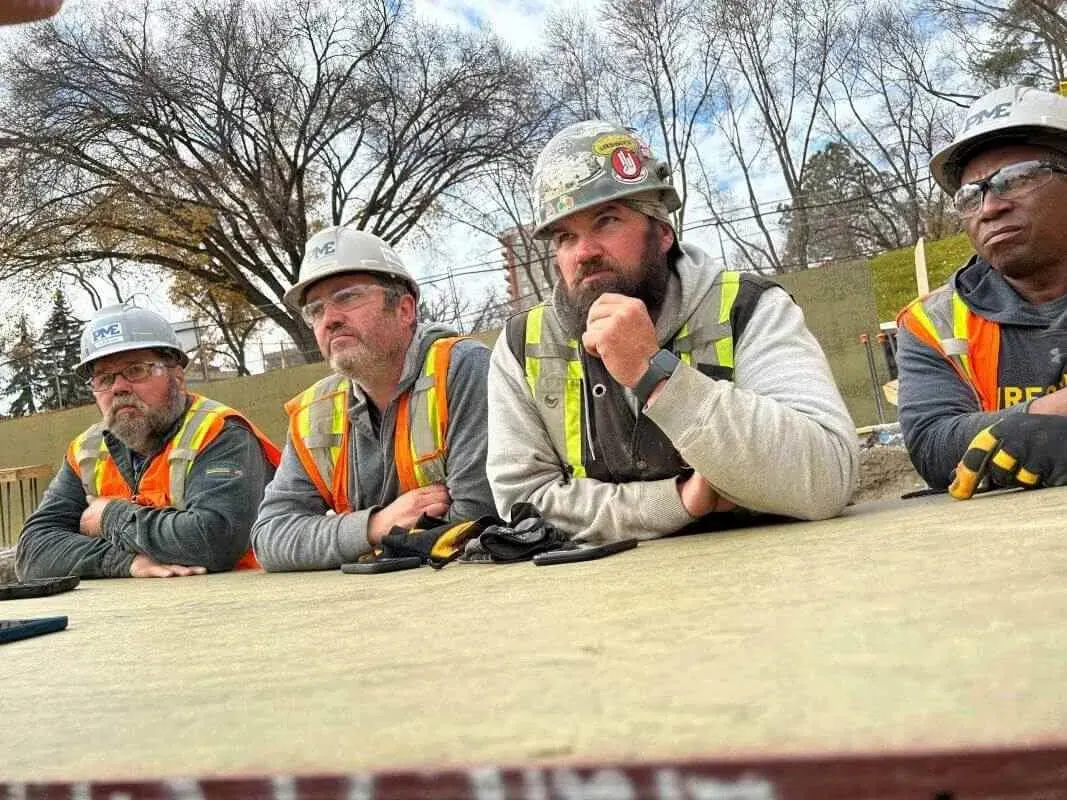 PME field crew in hard hats and high-visibility vests at outdoor toolbox talk table