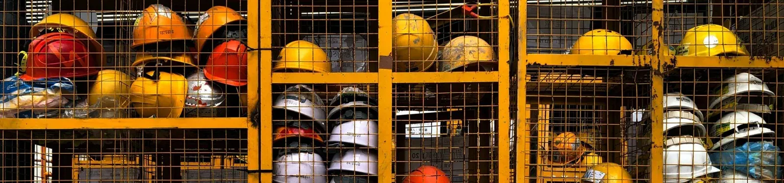 Yellow storage racks filled with worn hard hats at an industrial construction site