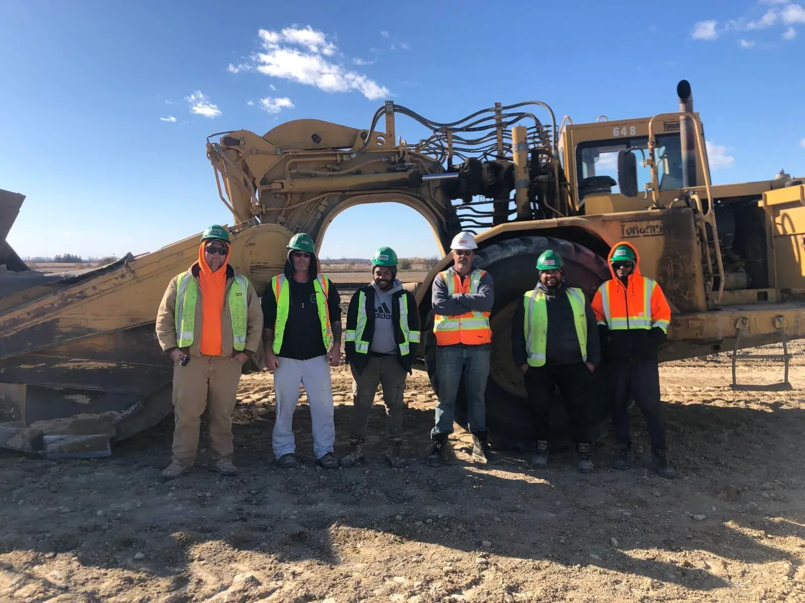Earthworks crew of six workers posed in front of a CAT scraper at a Crewscope client jobsite